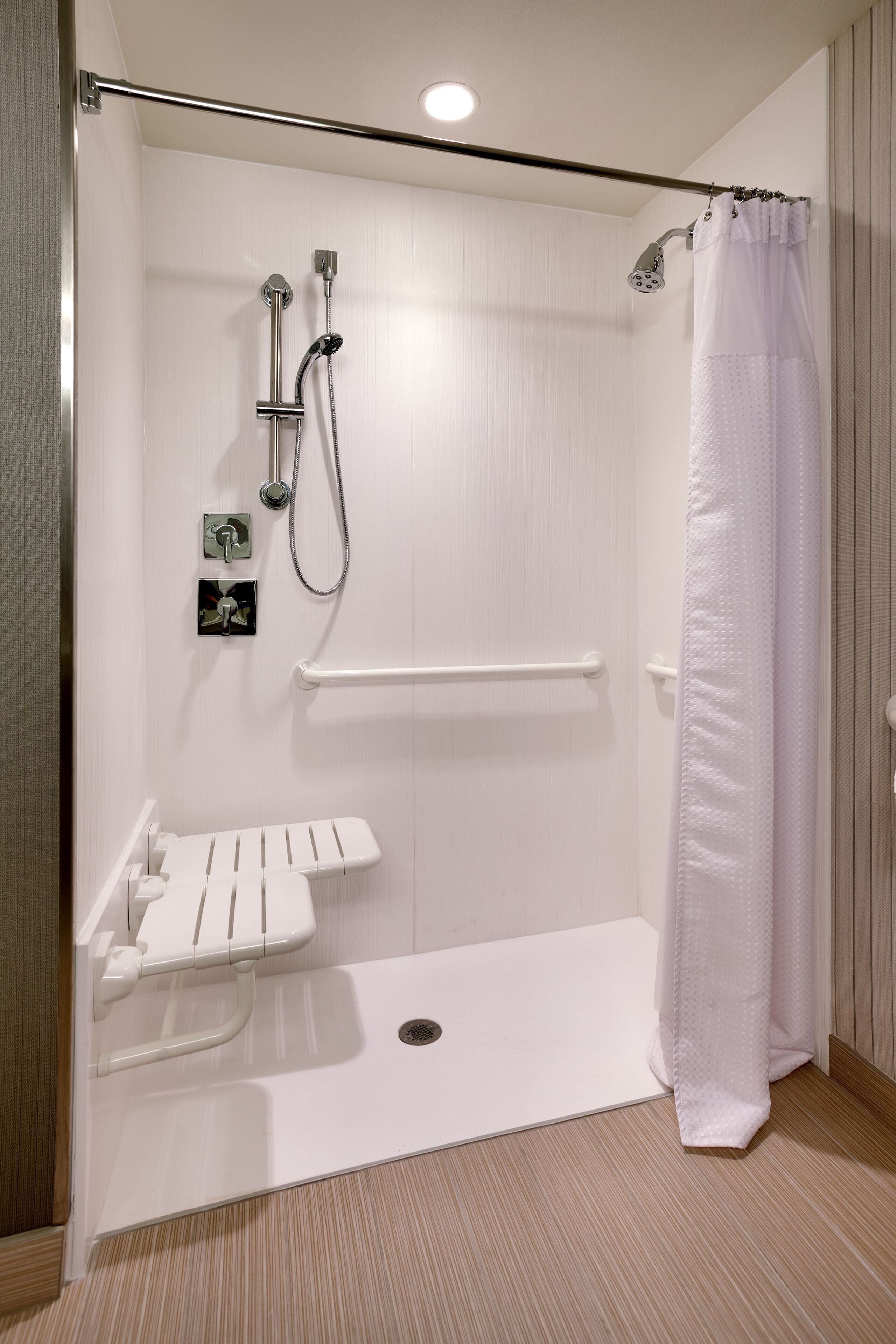 Une douche à l’italienne avec un rideau de douche blanc, une barre d’appui et un lavabo blanc doté d’un porte-serviettes.