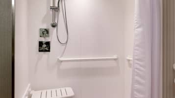 Een douche zonder opstaprand, met een wit douchegordijn, een handgreep en een wit wastafelmeubel met een handdoekhouder.
