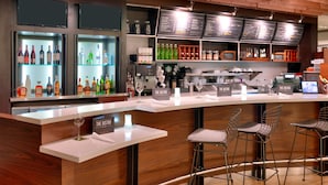 A bar area with a white countertop, shelves with bottles, and bar stools. - Courtyard Salt Lake City Downtown (Salt Lake City)
