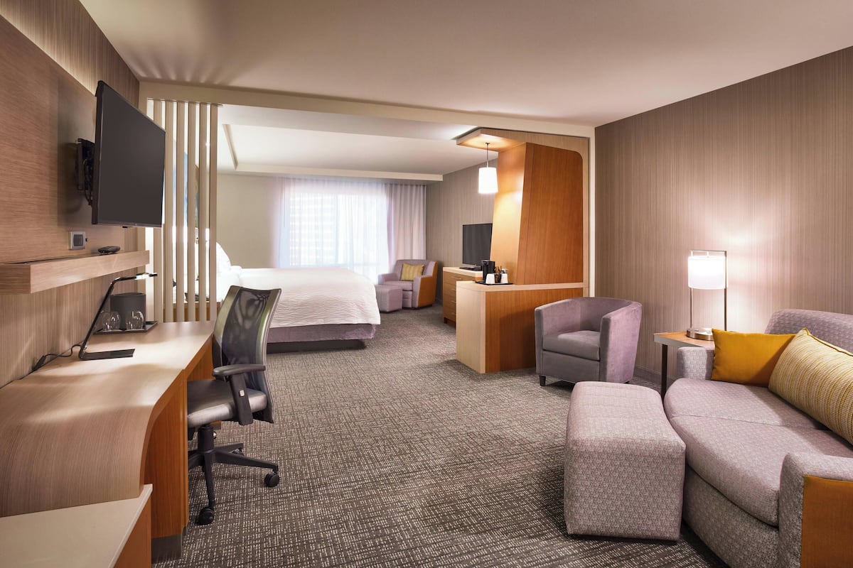 Ein Hotelzimmer mit Bett, Schreibtisch, Sessel, Sofa und einem an der Wand montierten Fernseher.