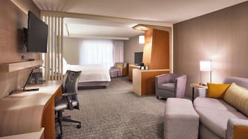 Habitación de hotel con cama, escritorio, silla, sofá y televisor montado en la pared.