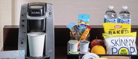 A coffee maker, a cup, snacks, and a water bottle on a desk.