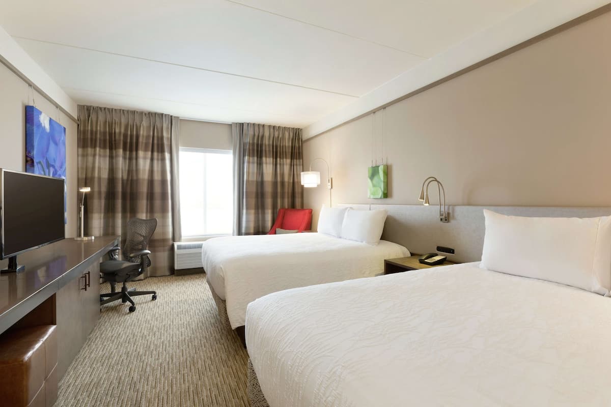 A hotel room with two beds, a desk with a computer, a chair, and a TV.