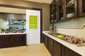 A breakfast buffet area with a sign detailing the menu, a self-service beverage station, and a kitchen area in the background. - Hilton Garden Inn Pittsburgh Airport South-Robinson Mall (Pittsburgh)