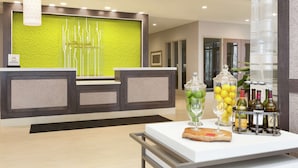 A reception area with a green textured wall, a reception desk, and a table with wine bottles and glasses. - Hilton Garden Inn Pittsburgh Airport South-Robinson Mall (Pittsburgh)