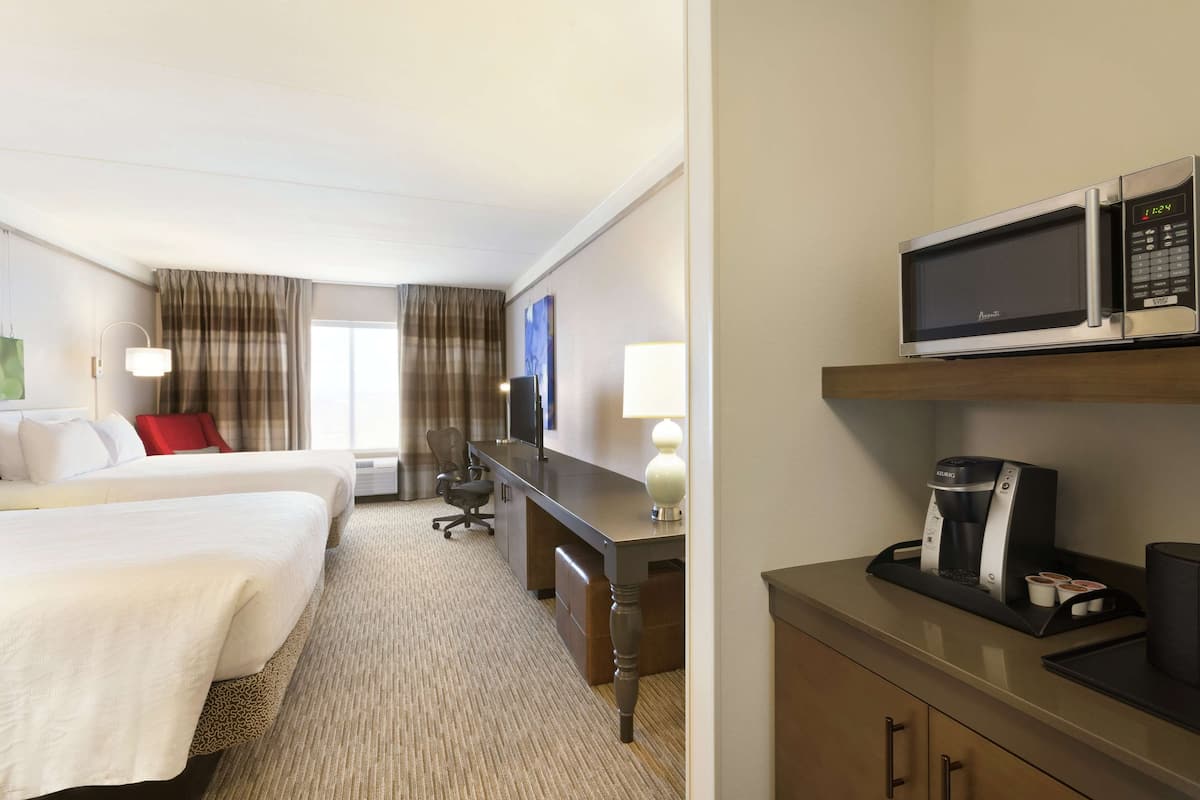 A hotel room with two beds, a desk with a coffee maker, a TV, and a microwave.