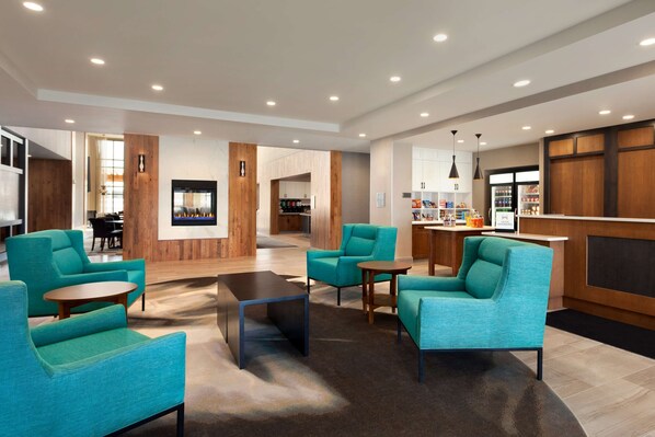 A modern lobby with teal armchairs, a coffee table, and a bar area with shelves.