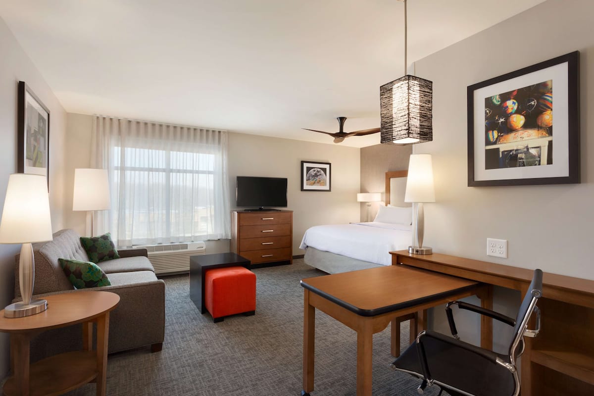 Habitación de hotel con cama, escritorio, silla, sofá, televisor y ventana con cortinas.