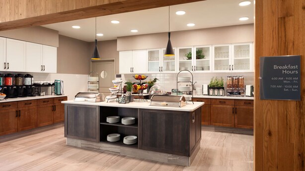 Una cocina moderna con armarios de madera, una isla central con un lavamanos y el horario de desayuno exhibido en la pared.