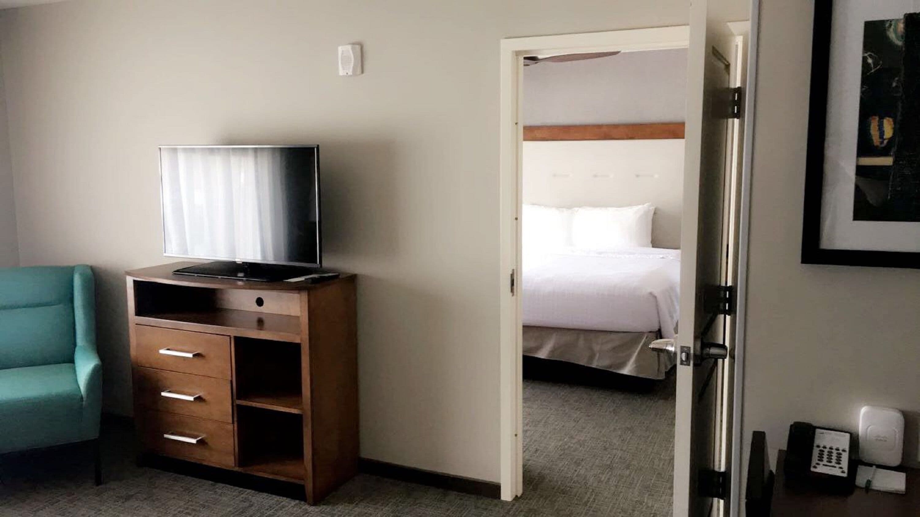 Una habitación de hotel con un escritorio de madera, un televisor, una cama y una puerta que da a otra habitación.