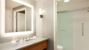 A modern bathroom with a large mirror, a sink with toiletries, and a glass-enclosed shower.