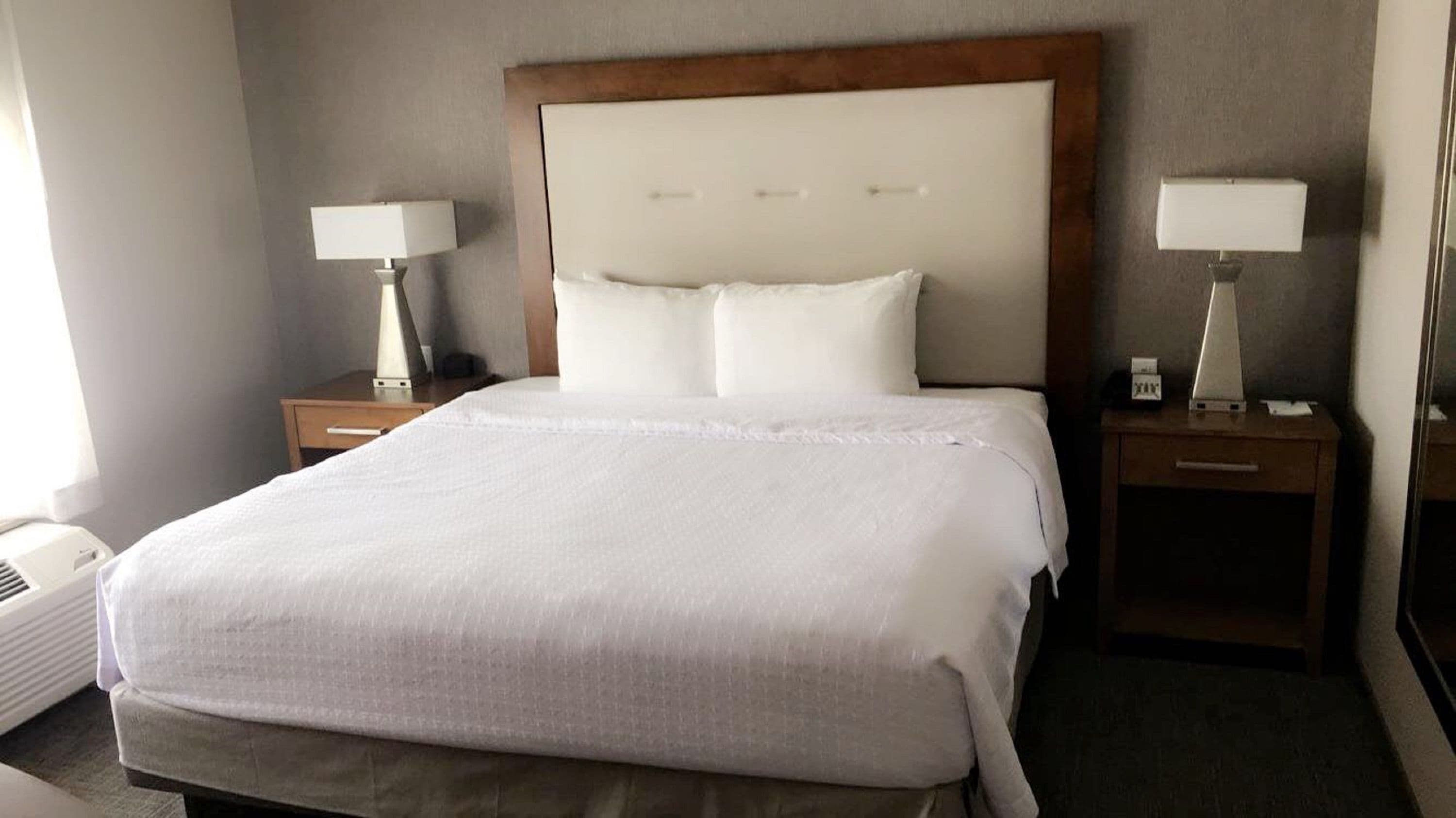 Ett hotellrum med en stor säng, två sängbord med lampor, en sänggavel i trä och ett vitt överkast.