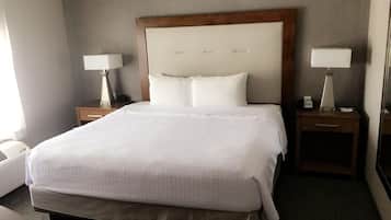 Habitación de hotel con una cama grande, dos mesitas de noche con lámparas, un cabecero de madera y una colcha blanca.