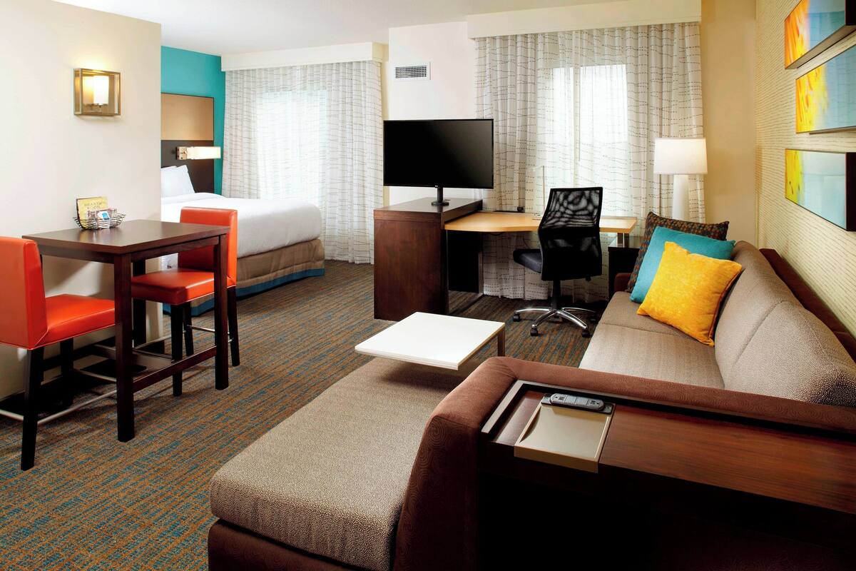 Habitación de hotel con cama, escritorio con computadora, sofá, mesa de centro y televisor.