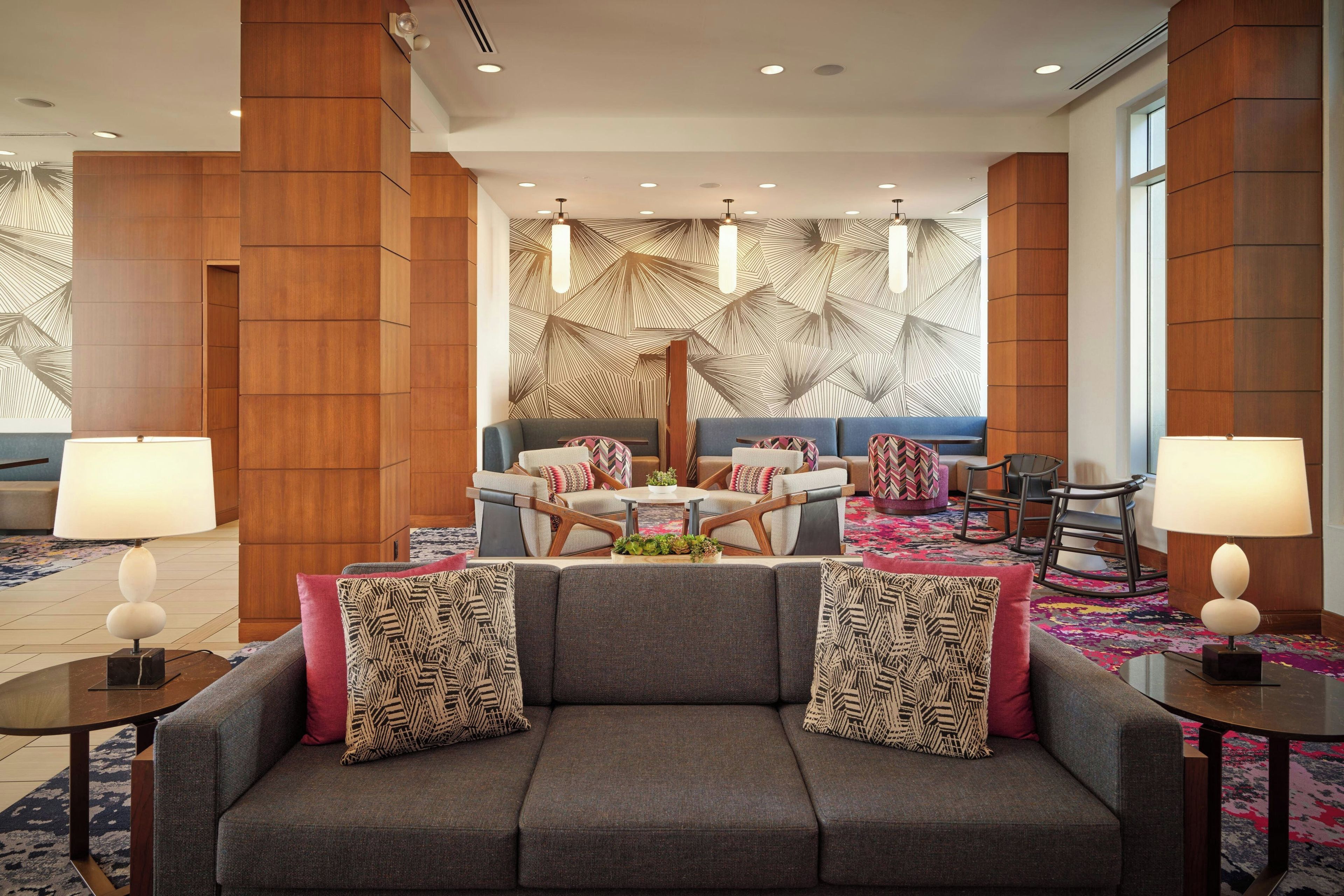 A modern lobby with a grey sofa, patterned cushions, a coffee table, and a patterned carpet.