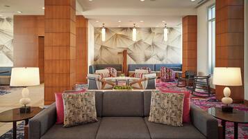 A modern lobby with a grey sofa, patterned cushions, a coffee table, and a patterned carpet.