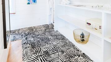 A room with a zebra-patterned rug, wooden beams on the ceiling, a white wall with a colorful abstract painting, and a white shelf with various items.