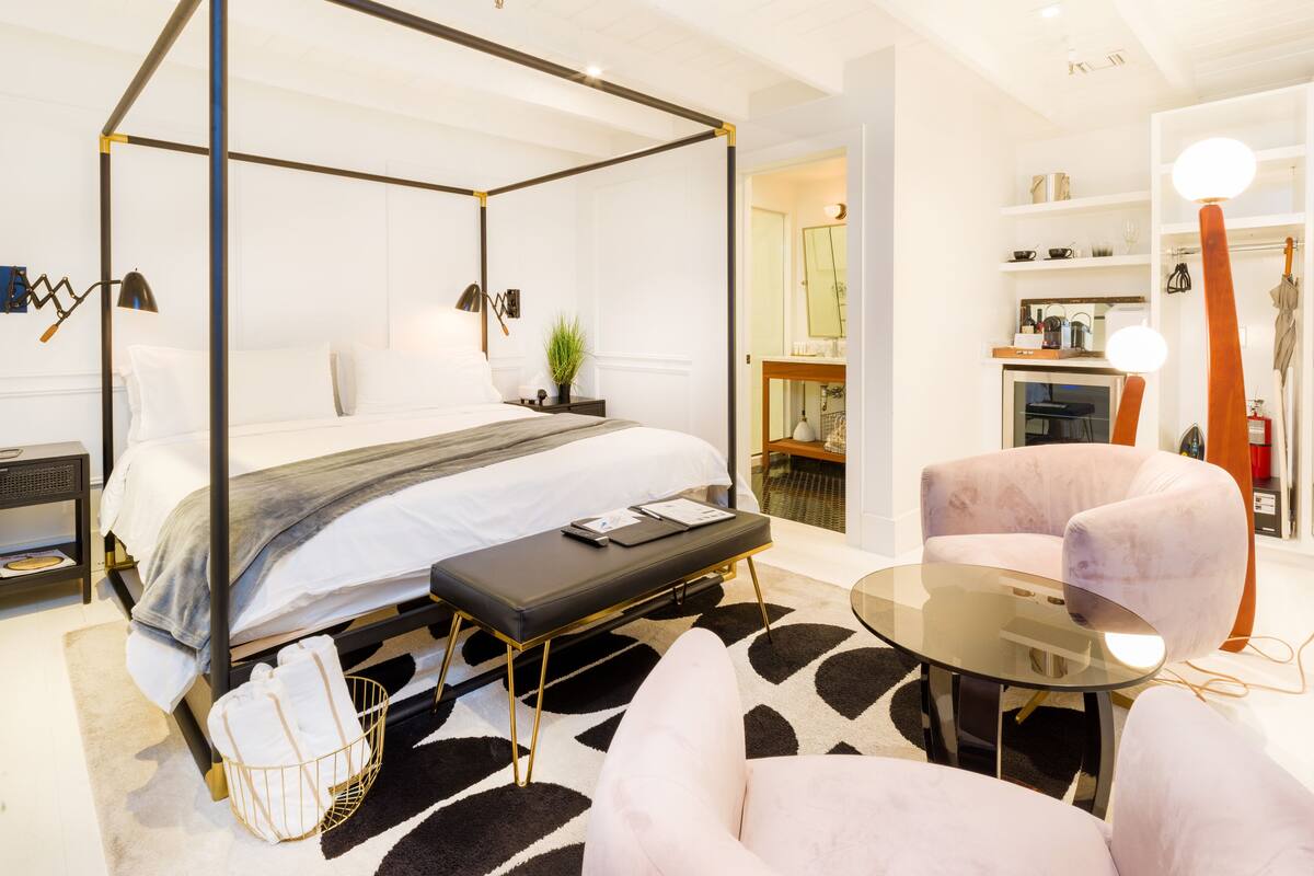 Une chambre d’hôtel moderne avec un lit à baldaquin, une petite table, une chaise et une table ronde en verre.