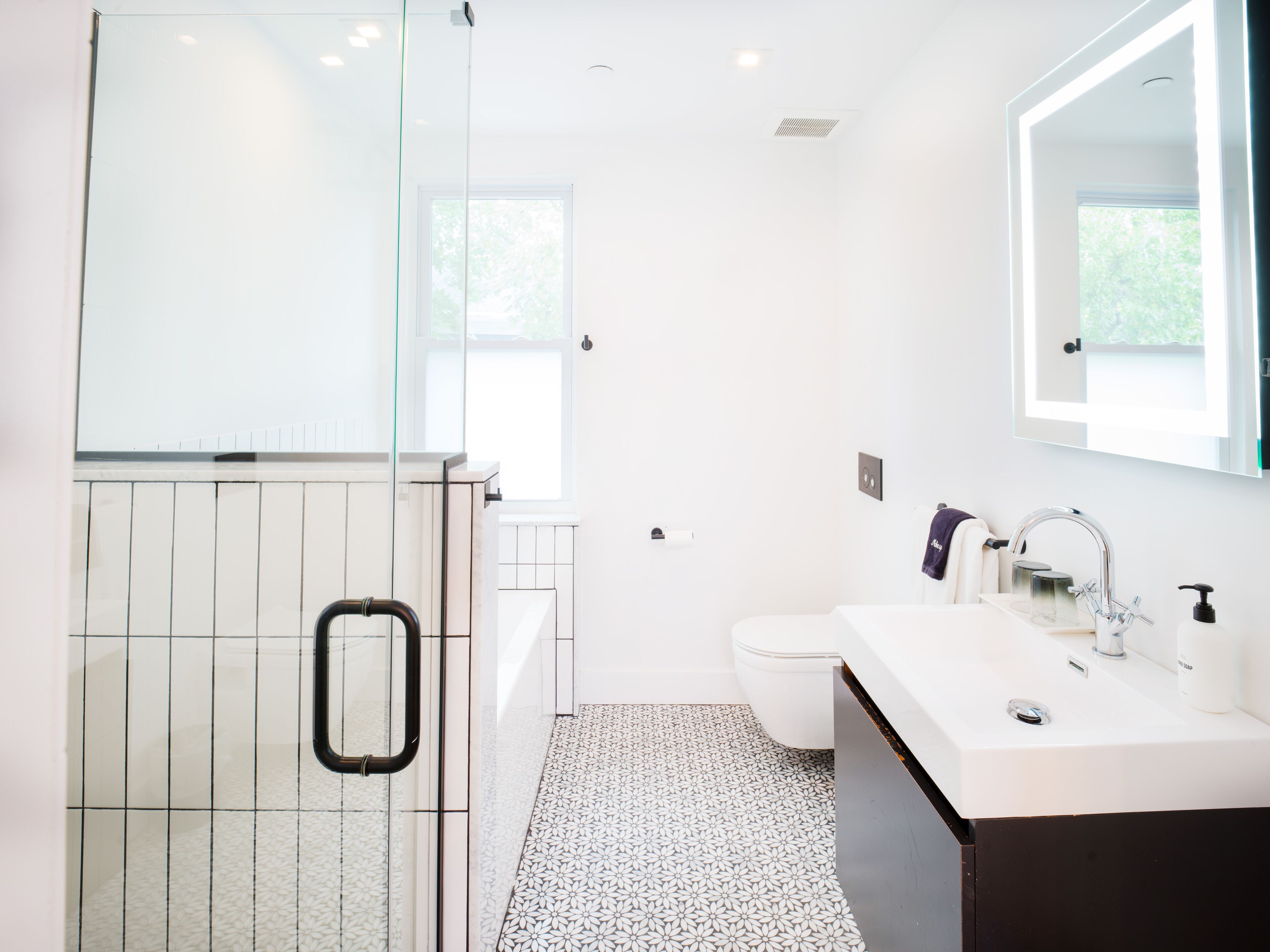 Une salle de bain moderne avec une douche à parois de verre, un lavabo blanc avec un miroir au-dessus et un carrelage décoratif.