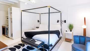 Ein modernes Hotelzimmer mit einem Himmelbett, einem kleinen Schreibtisch, einem blauen Sessel und einer Topfpflanze.