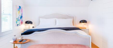 A bedroom with a bed, bedside tables, a bench, a zebra-patterned rug, and exposed wooden beams.