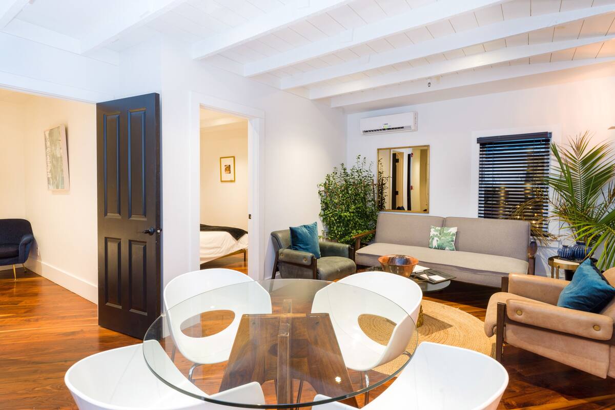 Un salon moderne avec une table en verre, des chaises blanches, un canapé et une table basse.