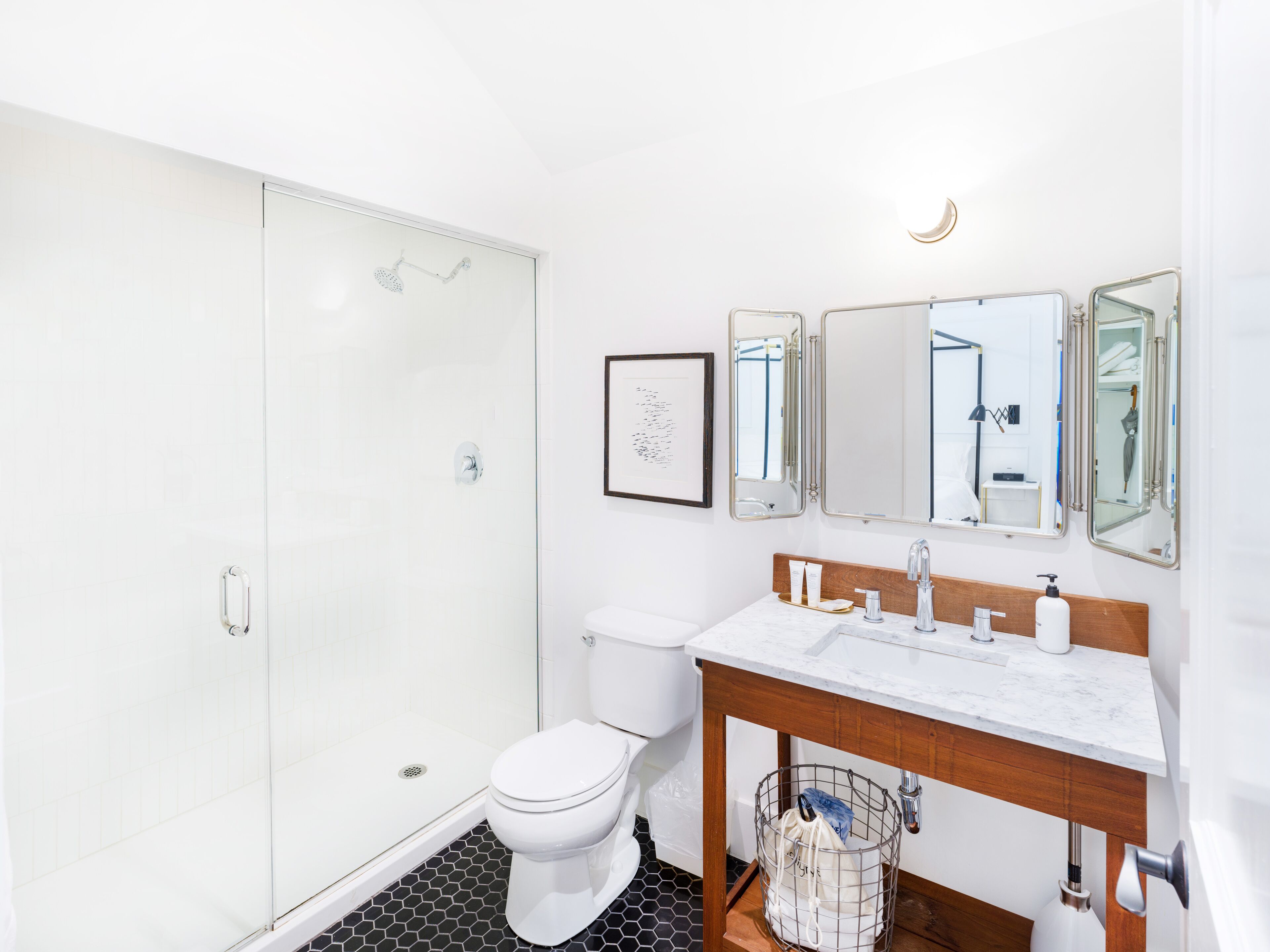 A modern bathroom with a glass shower enclosure, a toilet, a sink with a wooden vanity, and a mirror with three panels.