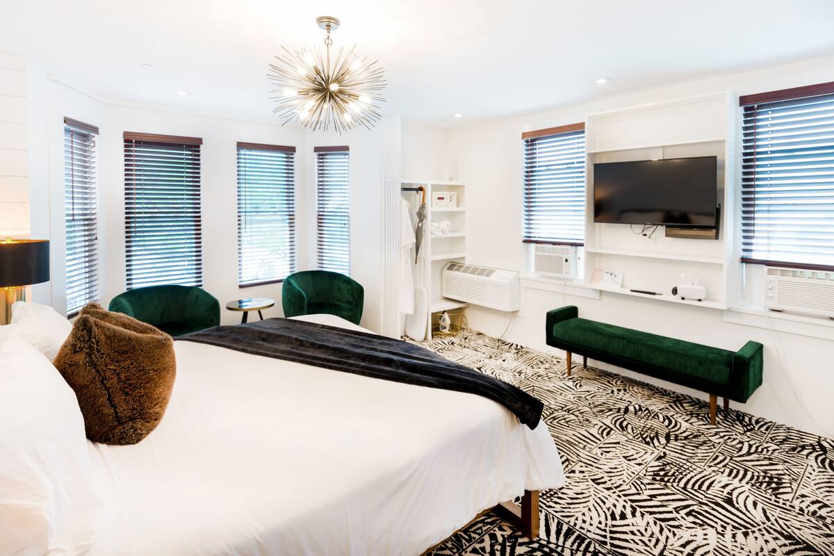 Une chambre d’hôtel moderne avec un grand lit, des fauteuils verts, un canapé vert, une télévision et un sol à motifs.