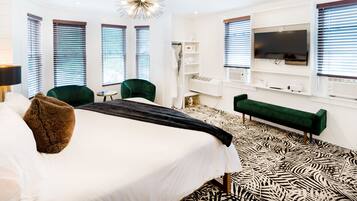 A modern hotel room with a large bed, green chairs, a green sofa, a TV, and a patterned floor.