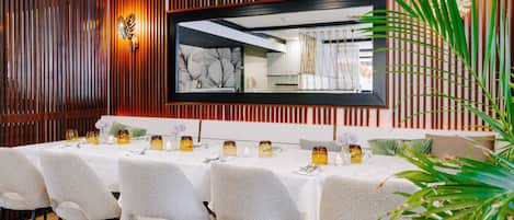 A dining area with a long table set for six, surrounded by chairs, and a large mirror on the wall.
