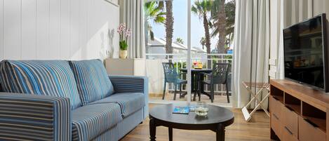 Un salon avec un canapé à rayures, une table basse, un téléviseur et un balcon aménagé avec du mobilier d’extérieur.