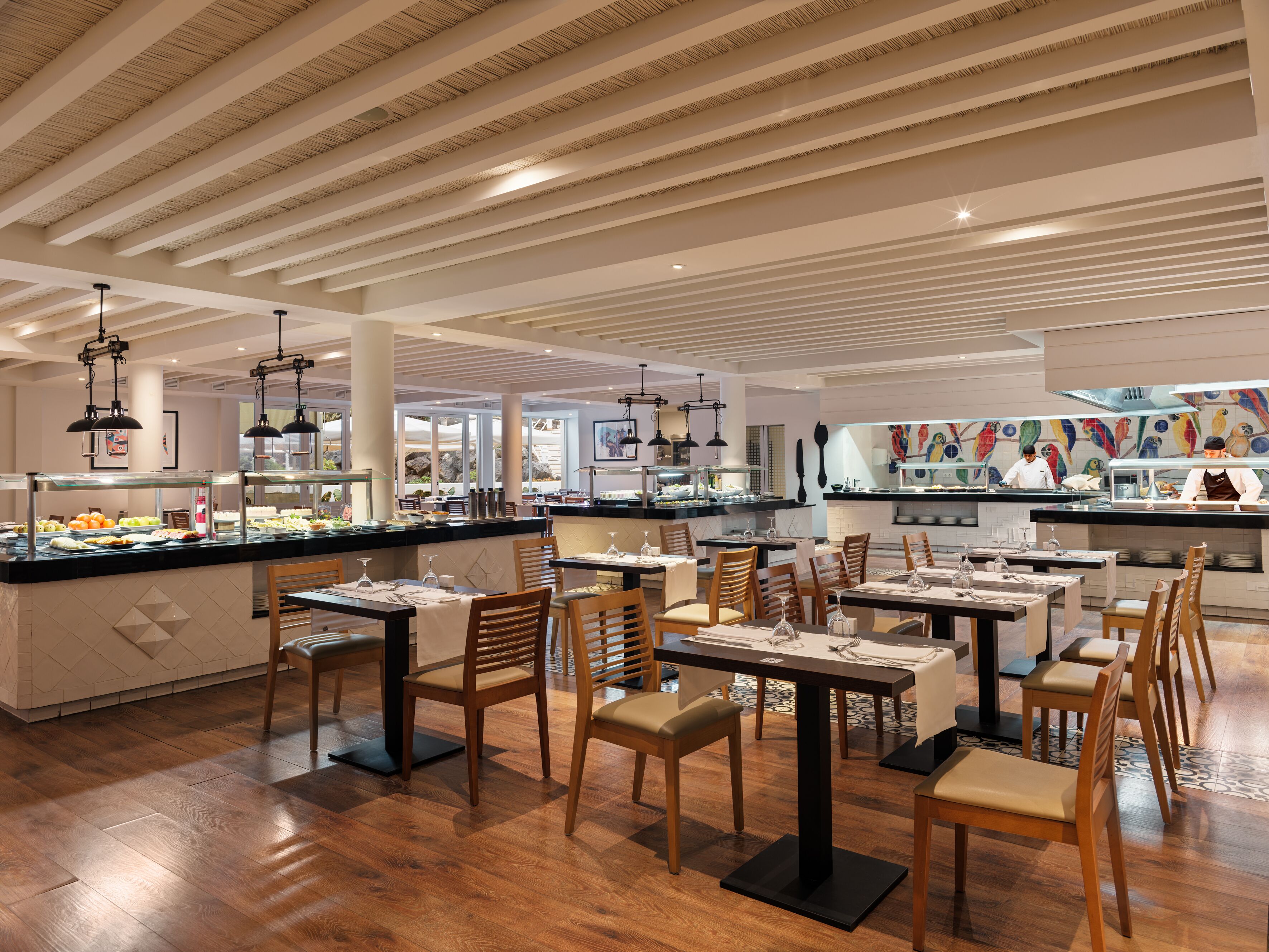 A modern restaurant with wooden flooring, black tables, and chairs.