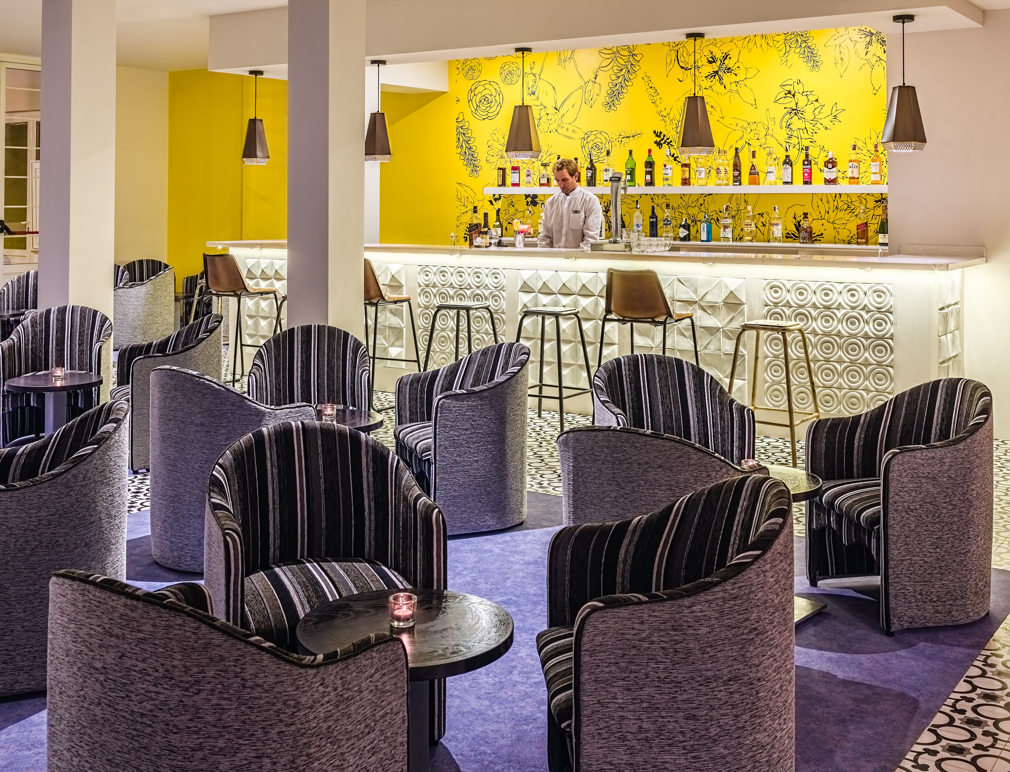 A bar area with striped chairs and a yellow wall with floral designs.