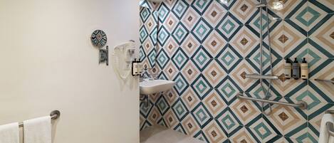 A bathroom with a patterned tile wall, a sink, a mirror, and a shower area.