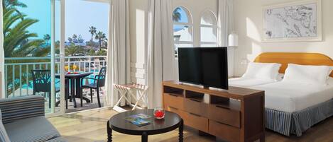 Habitación de hotel con cama, televisor, escritorio, silla, una mesita y balcón con vista a la piscina.