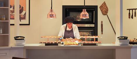 Un restaurant où le chef prépare les plats devant les clients, un buffet proposant divers plats et une salle à manger avec des tables dressées pour accueillir les convives.