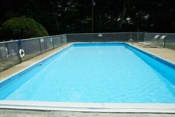 Una piscina rectangular con superficie de agua azul cristalina, rodeada por una cerca de metal y una plataforma de hormigón.