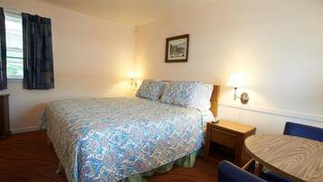 Habitación de hotel con cama, lámparas de noche, un cuadro en la pared, una mesita y una silla.