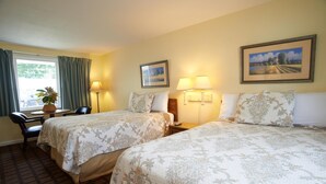 Habitación de hotel con dos camas, un escritorio, una silla, un ventanal con cortinas y dos lámparas de pared.