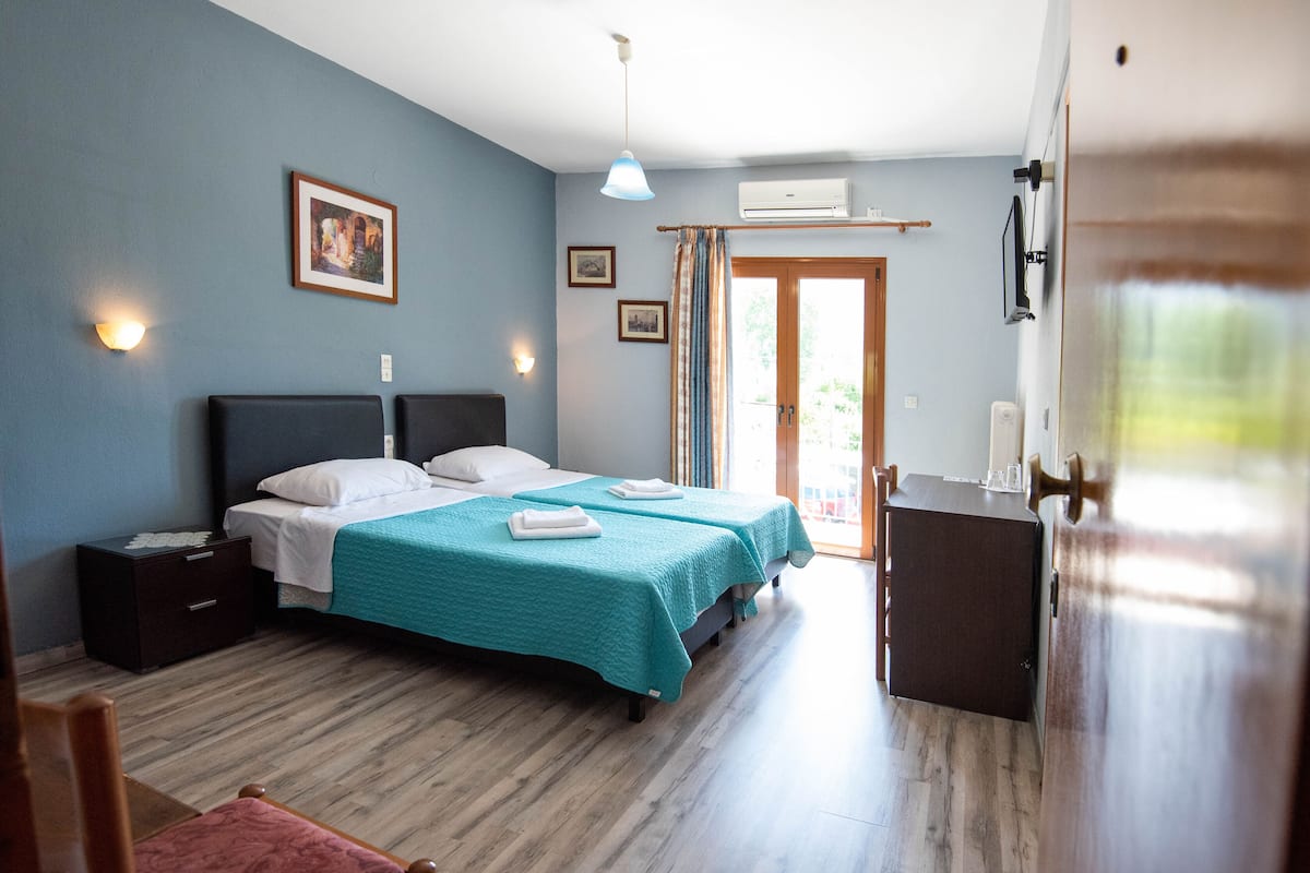 A bedroom with two beds, a nightstand, a desk, and a door leading to a balcony.