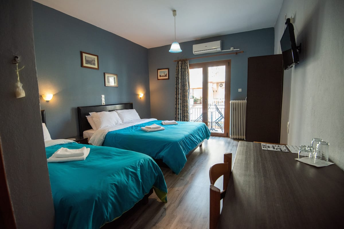 A hotel room with two beds, a wooden table, and a view of the outside balcony.