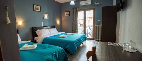 A hotel room with two beds, a wooden table, and a view of the outside balcony.