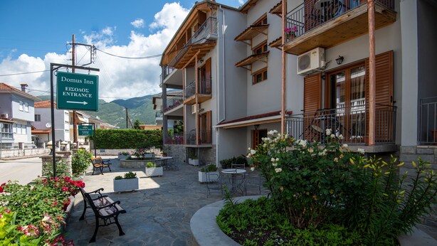A hotel entrance with a sign, outdoor seating, and a garden area. - Domus Inn (Ioannina)