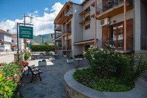 Entrada de un hotel con letrero, mesas al aire libre y un jardín.