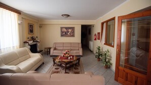 A living room with a beige sofa, a coffee table with a floral centerpiece, and a fireplace. - Domus Inn (Ioannina)
