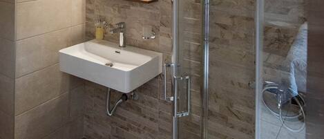 A modern bathroom with a glass-enclosed shower, a sink with a mirror above it, and a wall-mounted heater.