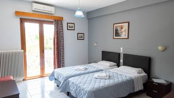 A hotel room with two beds, a radiator, a window with curtains, a ceiling fan, and a wall-mounted air conditioner.