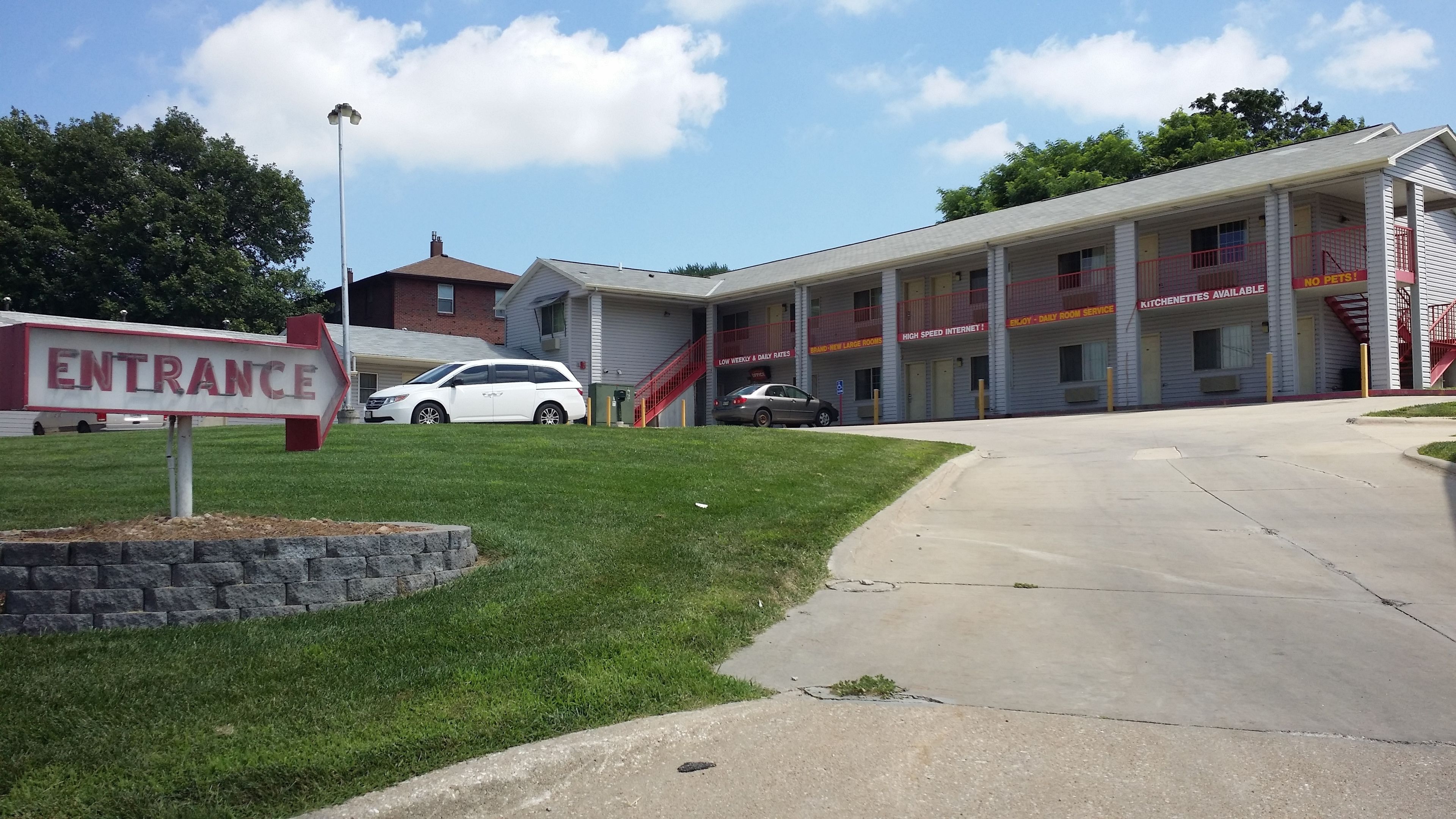A building with an entrance sign, a covered walkway, and a parking area with cars.