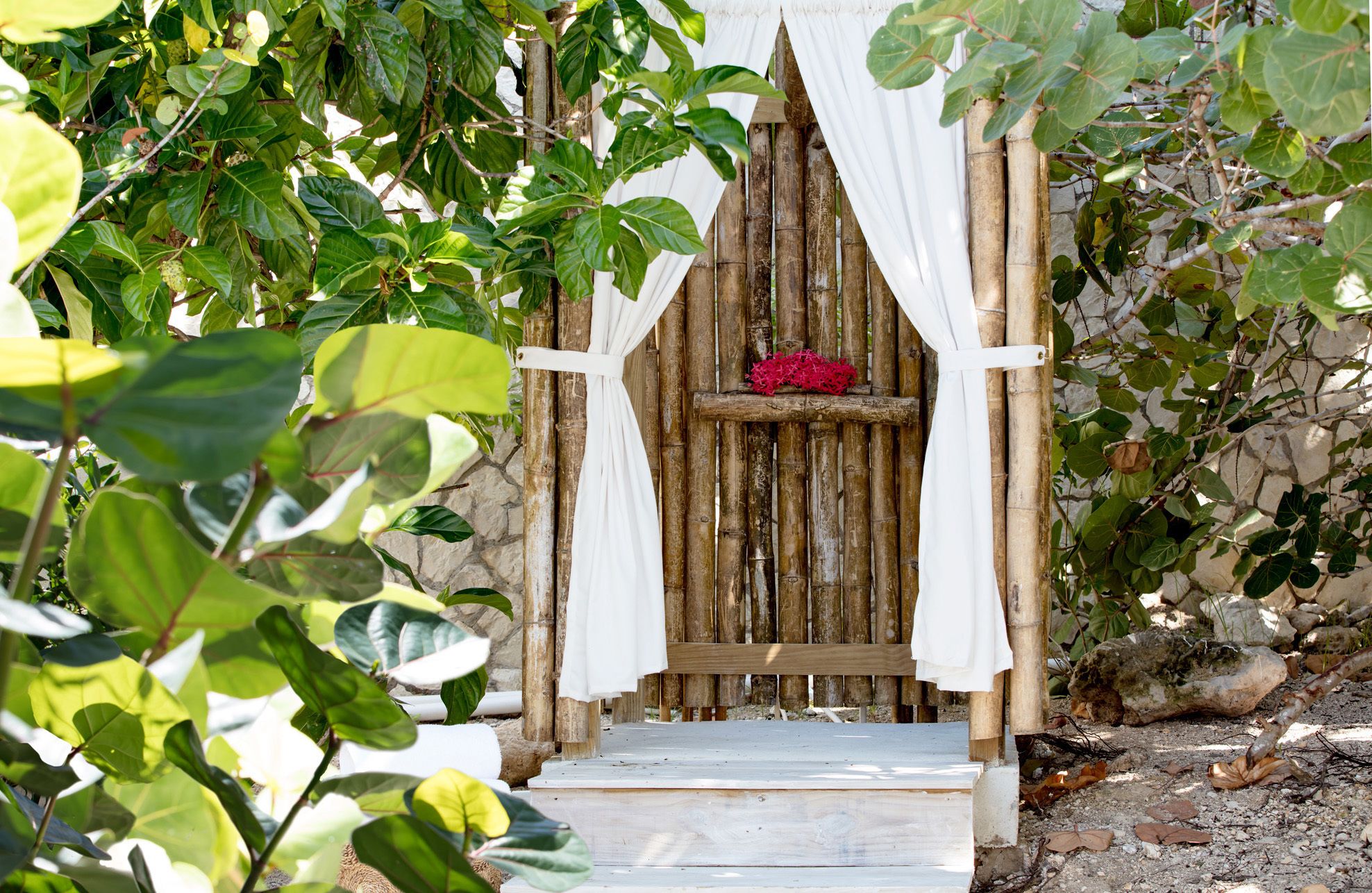 A wooden structure with white curtains and a shelf with red flowers.