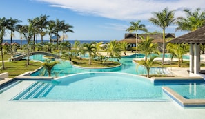 A resort pool area with multiple swimming pools, palm trees, and beach views. - The Cliff Hotel (Negril)